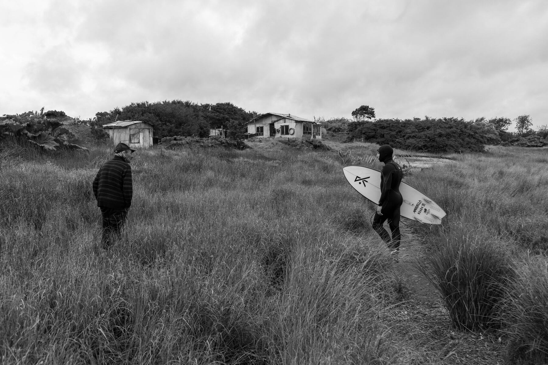 Dos surfistas caminando por el pasto hacia la playa