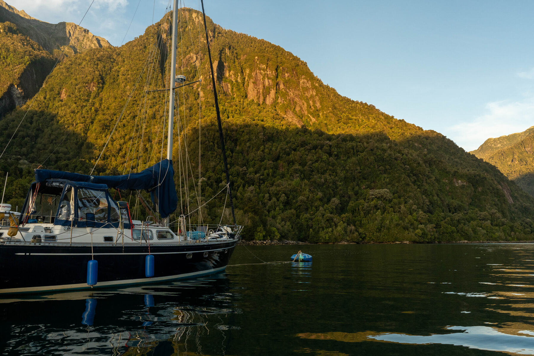 Velero fondeado bajo cerros verdes iluminados por el atardecer en un fiordo patagónico